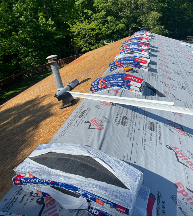 Roof with synthetic underlayment on one side and exposed decking on the other during new roof installation.