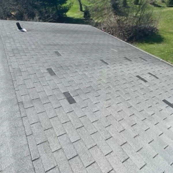 Old 3-tab shingled roof with parts of the shingles blown off.