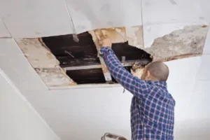 Man on ladder inspecting ceiling damage caused by leaking roof